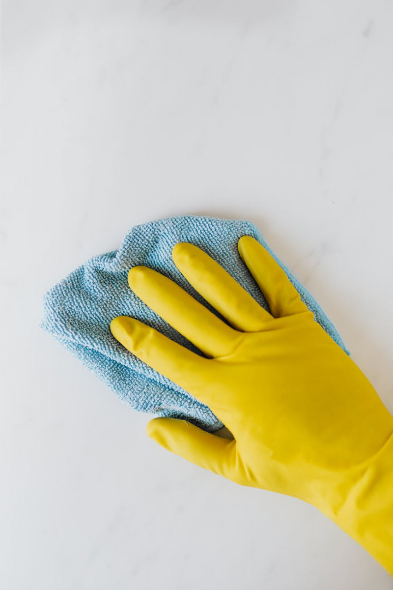 crop unrecognizable person in yellow gloves cleaning white surface
